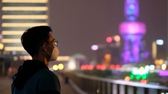 A young man wearing surgical mask looking at Oriental Pearl TV Tower in Shanghai at night